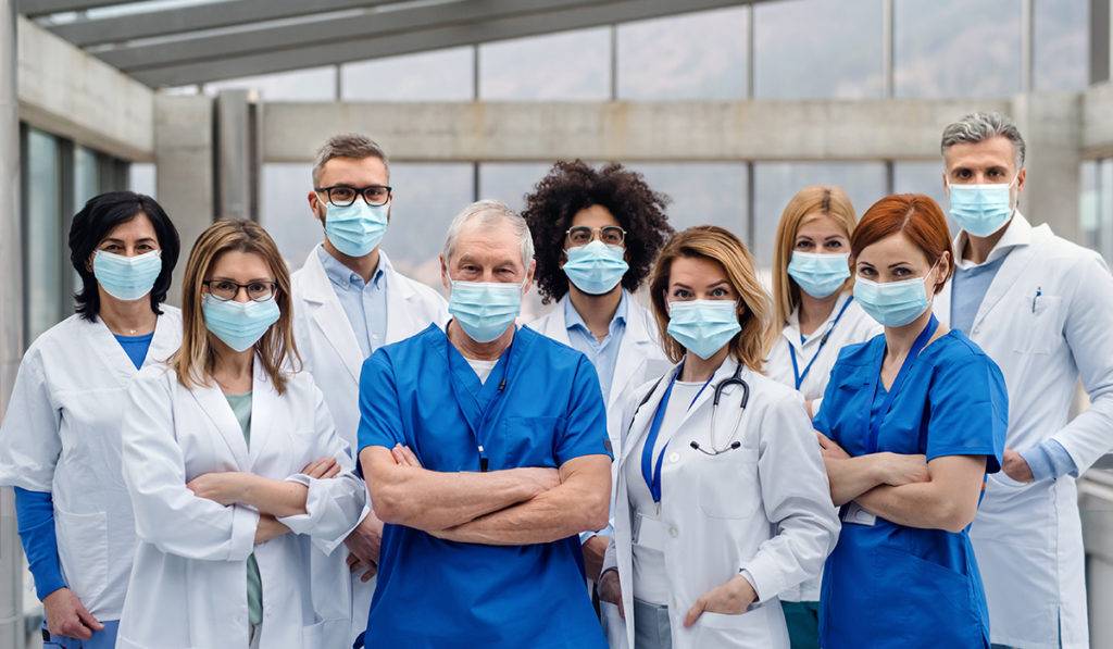 A group of masked nurses and doctors in front of an office building