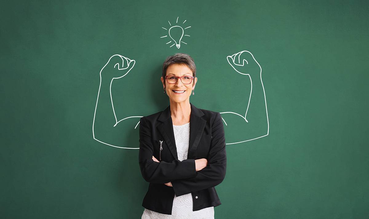Woman standing in front of chalkboard with drawing of muscular arms behind her to symbolize motivation